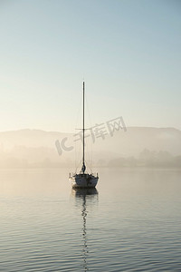 电风摄影照片_航行游艇的美丽的不插电风景图像坐在平静的湖水在湖区在和平的薄雾秋天日出