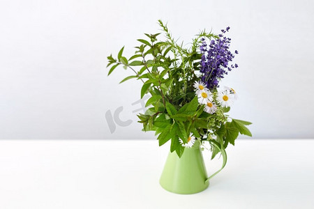 绿党摄影照片_园艺，植物和有机概念—一束草药和鲜花在绿色壶在桌子上。一束草药和鲜花在绿色壶在桌子上