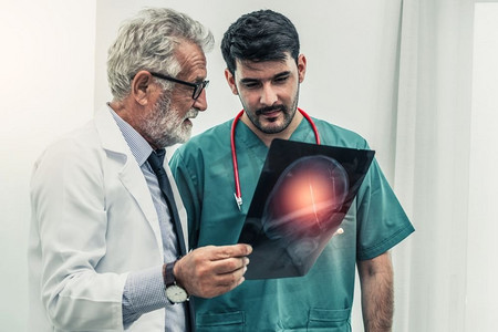 老年大脑摄影照片_医生在医院与另一个外科医生一起处理病人头部的x光片。医疗保健和医务人员服务理念。