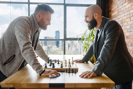 象棋选手互相对视。’两名棋手在室内完成智力竞赛。木桌棋盘