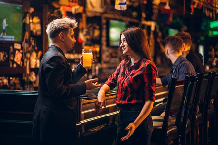 年轻人手里拿着啤酒杯，在体育酒吧的酒吧柜台与妇女谈话，足球迷的快乐休闲