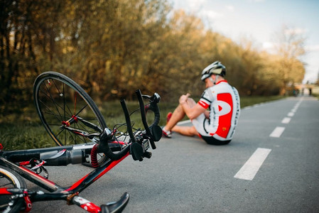一名骑自行车的男子在自行车道上骑车时从自行车上摔下来，撞到膝盖。一名骑自行车的男子从自行车上摔下来，撞到膝盖
