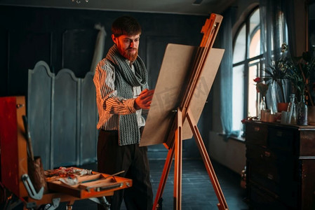 男画家手里拿着画笔在画架前。油画、画笔绘画。画架前有画笔的男画家