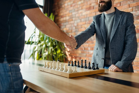 象棋选手在比赛前握手。两名男棋手在室内开始了智力战。国际象棋选手在比赛前握手