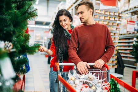 夫妇购买圣诞树在超市。十二月购物，选择节日装饰品。夫妇购买圣诞树在超市