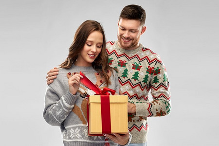 人物和节日概念-丑陋毛衣派对上带着圣诞礼物的幸福夫妇肖像。穿着圣诞毛衣和礼品盒的幸福夫妇