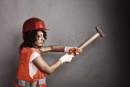 建筑工人的工具摄影照片_性别平等和女权主义。性感女孩戴着安全头盔橙色背心拿着锤子工具。做建筑工人的漂亮女人。