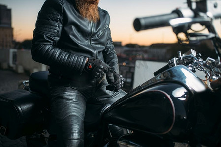 日落时分，摩托车手在城市里的摩托上摆姿势，经典的直升机。复古自行车，自由生活方式，骑自行车