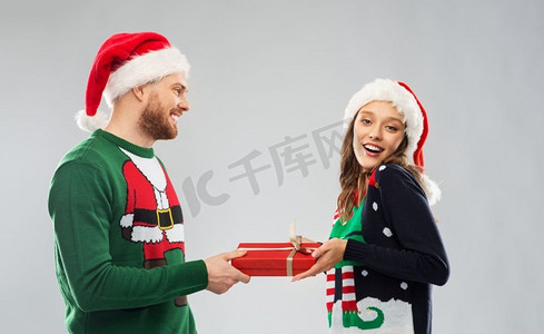 人和假日概念—快乐夫妇在圣诞老人帽子与圣诞礼物在丑陋的毛衣党。快乐的夫妇在圣诞毛衣与礼品盒