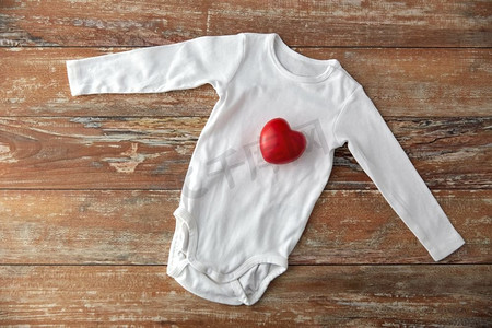 婴儿衣服，婴儿时代和服装概念—紧身衣与红心玩具在木桌子上。婴儿紧身衣与红心玩具在木桌上