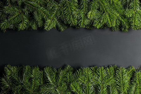 圣诞边框用新鲜的冷杉树枝排列在黑色纸张背景上，复制文本空间。冷杉树枝的圣诞边框