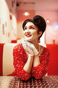 迷人的别针女孩与红色的嘴唇坐在复古咖啡馆，50美国时尚。圆点连衣裙，复古风格