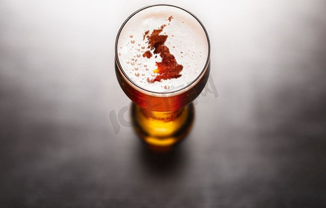 黑色剪影元素摄影照片_英式啤酒概念，黑色桌子上的啤酒杯泡沫上的英国剪影。美国国家航空航天局提供的这张图片的元素。英国啤酒概念