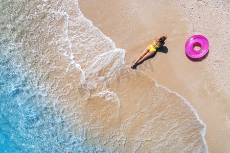 日落时分,在海边的沙滩上,带着粉红色游泳圈的美丽年轻女子的鸟瞰图.