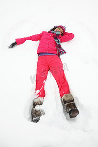 在一个阳光明媚的冬日假期的雪的美丽的快乐的年轻女子。年轻女子躺在雪地上