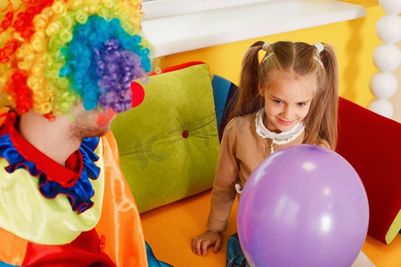 有趣的小丑把气球给小女孩。在生日派对上穿着五颜六色的服装的小丑。有趣的小丑给小女孩气球