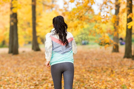 健身，运动和健康的生活方式概念—年轻女子跑步在秋天公园。在秋天公园跑步的年轻女子