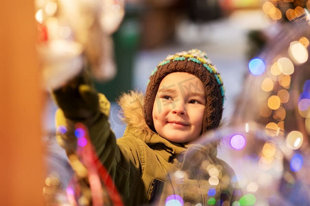 节日、童年和人的概念--冬天的傍晚圣诞集市上的小男孩。冬天圣诞集市上的快乐小男孩