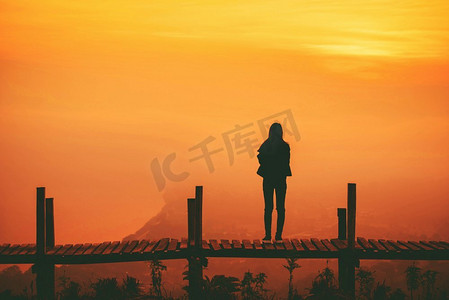站在山上木桥上的剪影女子和夕阳黄天的背景