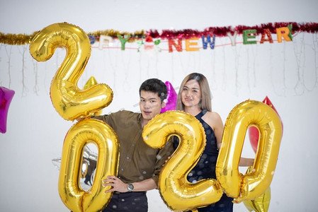 快乐的年轻夫妇与2020气球在背景。新年庆祝活动