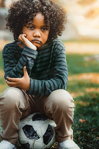 坐在公园里的不开心无聊的小非洲裔美国人孩子。男孩表现出消极情绪。儿童问题概念。