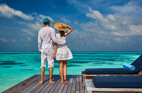 一对夫妇在马尔代夫的热带海滩码头上穿着白色衣服