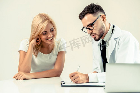 男医生在医院办公室与女病人交谈，同时在桌子上写下病人的健康记录。医疗保健和医疗服务。
