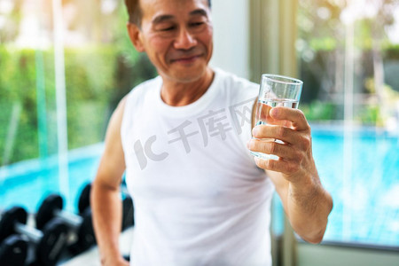 喝矿泉水摄影照片_老年人运动后到健身中心喝矿泉水。老年人健康生活方式老年人在健身中心喝矿泉水。