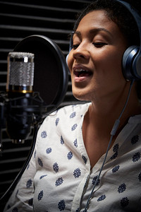 女歌手在录音室戴耳机对着麦克风唱歌