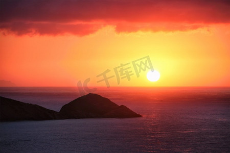 夕阳落下摄影照片_海上落日。海景日落与小岛。太阳在海里落下。克里特岛，希腊。希腊的海上夕阳