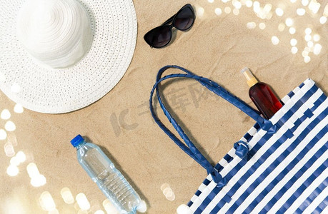 度假，旅行和夏季概念—沙滩袋，防晒霜，太阳镜和帽子在沙滩上。沙滩袋，防晒霜，太阳镜和帽子在沙滩上