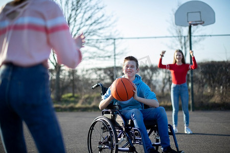 少年男孩在轮椅上打篮球与朋友