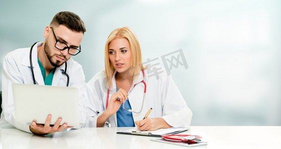 全科医生摄影照片_医生在办公室用笔记本电脑工作，同时在医院与另一位医生讨论。医疗保健和医生服务。