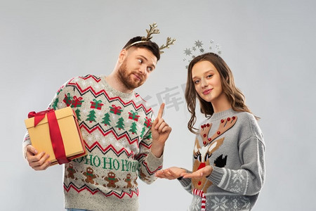 人物和节日概念-丑陋毛衣派对上带着圣诞礼物的幸福夫妇肖像。穿着圣诞毛衣和礼品盒的幸福夫妇