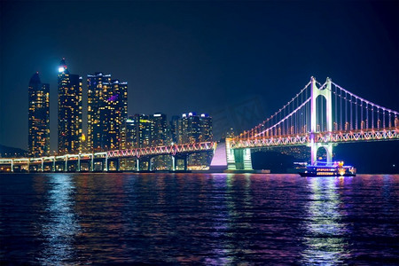 广安桥摄影照片_广安桥和摩天大楼在夜里被照亮。韩国釜山。夜晚的广安桥和摩天大楼。韩国釜山