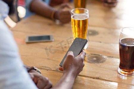 喝啤酒摄影照片_人和技术概念—人与智能手机喝啤酒和阅读消息在酒吧或酒馆。男子与智能手机喝啤酒在酒吧或酒馆