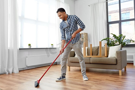 清洁、家务和家政概念--印度男人在家里扫地。家里拿着扫帚打扫地板的男人