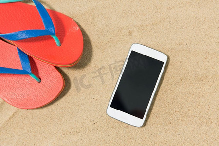 科技、度假和暑假概念--沙滩上的智能手机和人字拖。沙滩上的智能手机和人字拖