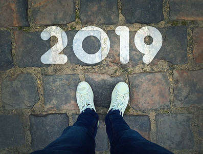 站在2019年起跑线旁边的白色运动鞋的人的顶视图在老式人行道背景上。开始新的一年挑战概念。 
