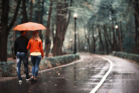 雨在秋天公园/年轻的25岁夫妇男人和女人走在伞下在潮湿的雨天，走十月情人