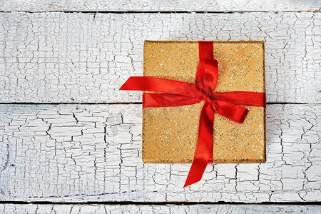 白色礼盒红色丝带摄影照片_礼物生日圣诞节礼物概念—黄金礼物盒与红色丝带在白色被画的木背景。俯视图。红丝带礼盒