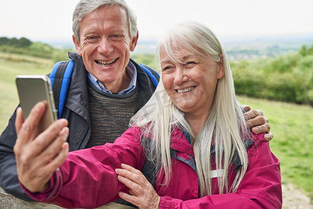微笑的老年夫妇徒步在农村站在门口和采取自拍手机     
