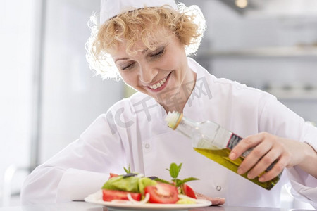 面带微笑的成熟厨师在餐厅的盘子里往沙拉上倒油