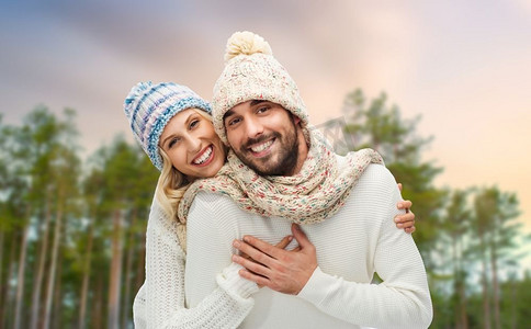 冬天，圣诞节和人概念—帽子和围巾拥抱在森林背景的愉快的夫妇夫妇拥抱在冬季森林背景