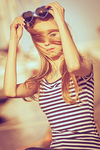 夏季时尚。肖像女孩在蓝色心形太阳镜享受夏天微风在日落在码头
