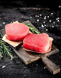生金枪鱼牛排放在迷迭香切菜板上。在黑色背景上。高质量的照片。生金枪鱼牛排放在迷迭香切菜板上。