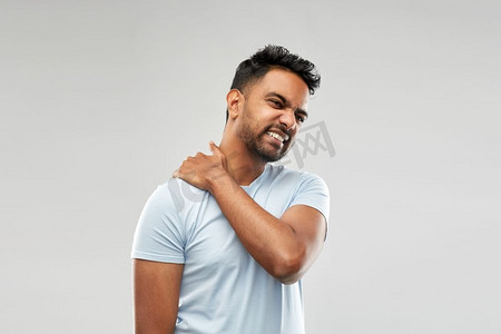 健康问题和人的概念—不健康的印度男子遭受脖子疼痛在灰色背景。不健康的印度男子遭受颈部疼痛