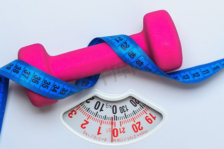 健康的生活方式健身减肥理念。特写镜头粉红色哑铃与蓝色卷尺在白色规模