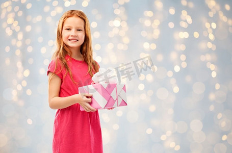 生日和人物概念-微笑的红发女孩带着礼品盒，背景是节日灯光。微笑的红发女孩带着生日礼物