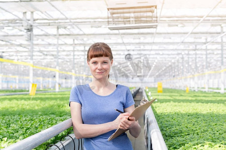 年轻女植物学家拿着剪贴板站在苗圃里的肖像